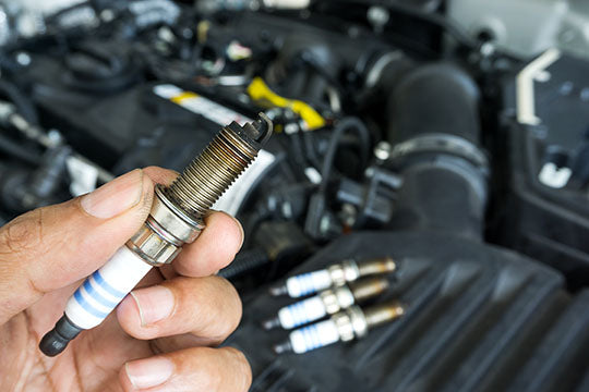 Mechanic holds an old spark plug over an engine bay